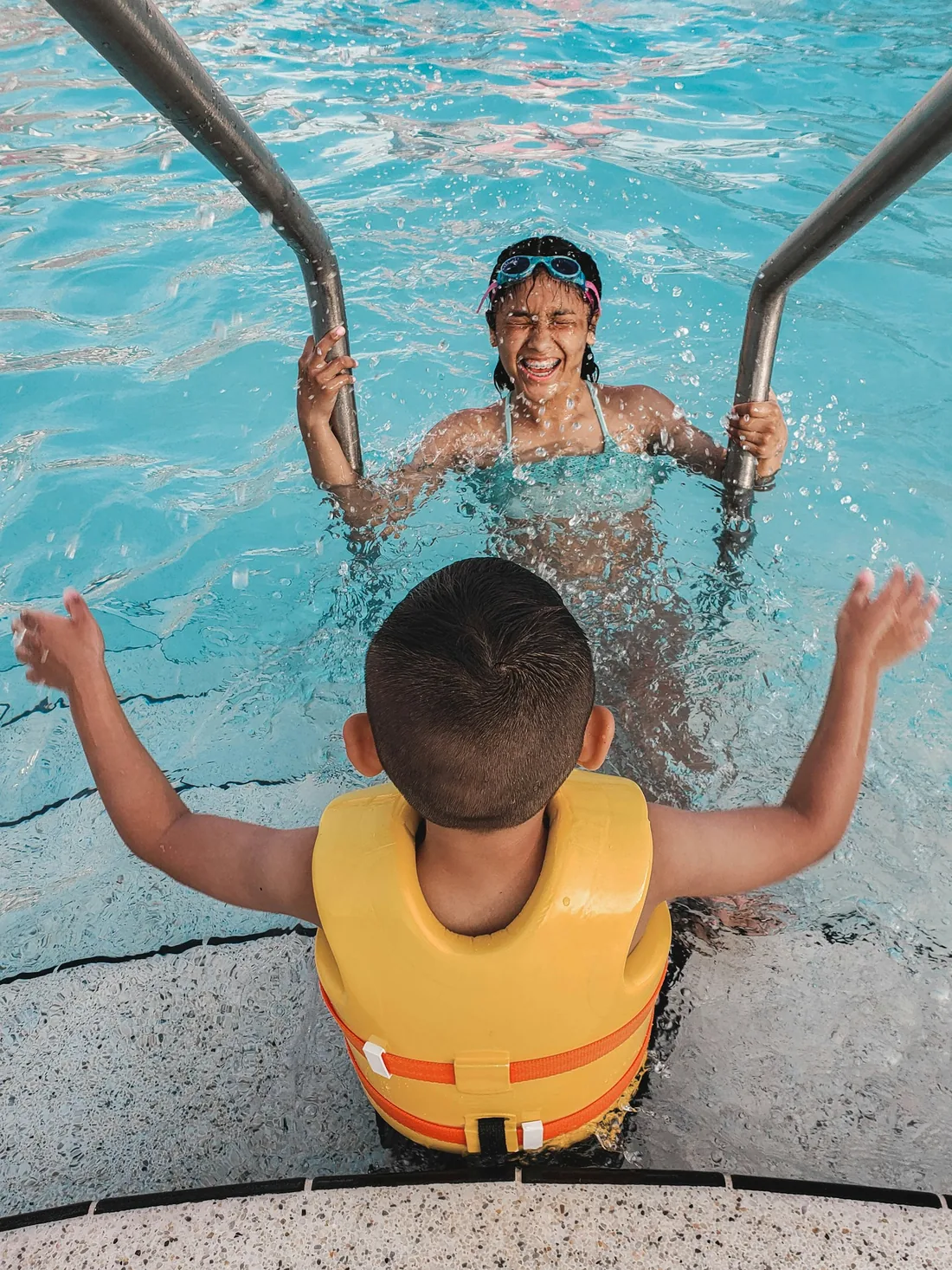 Swim instructor guiding a young child wearing a life jacket into the pool