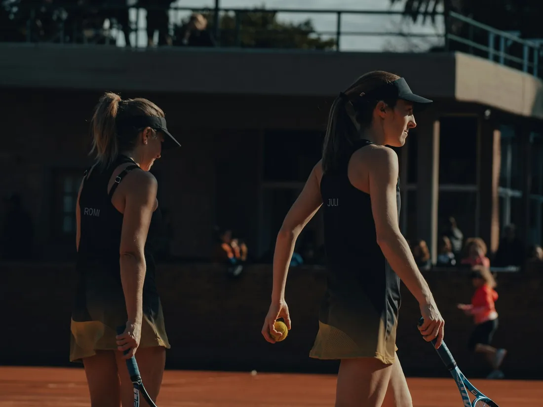 Two players carrying rackets across a clay tennis court